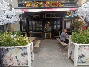 From street, facing venue. Planters on both sides. Seating behind. Path in middle. Doorway at back.