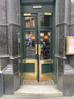 Access via double glass door with dark green frame. Pull open via metal handles in center.