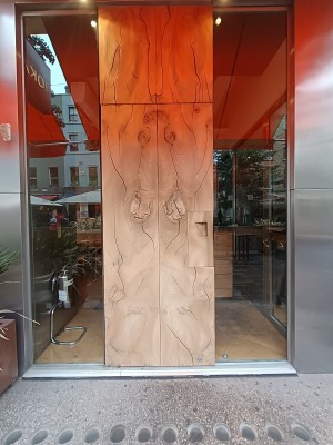 Brown wooden door with handle on right. Glass walls around doorway. Pull to open.