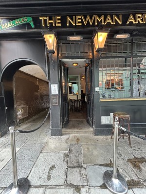 From street facing venue. Path ahead. Rope barrier on left. One step up to glass doors with black frames. Push via vertical handles in centre to open.