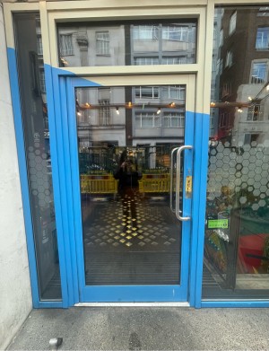 Glass door with blue and white frame ahead. Silver vertical handle to right. Pull to open.
