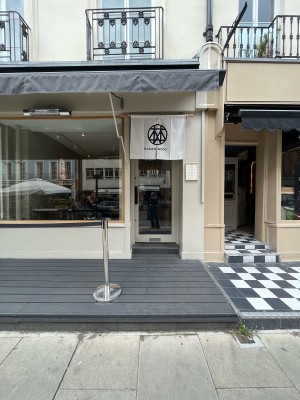 From pavement facing venue. Path ahead to single glass door in green wooden frame. Push silver metal handle from left to open. Queue divider on left.