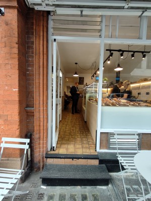 Facing white framed single glass door. Push white metal handle on right to open.