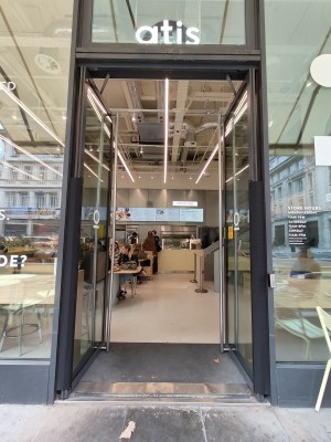 Facing black framed double entrance door. Push silver metal vertical handles in centre or button on right of door for door to open outwards.