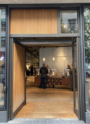 Access via double door. Left wide wooden one and right narrow glass one with black frame. Push open via vertical metal handrail on right of wide door.