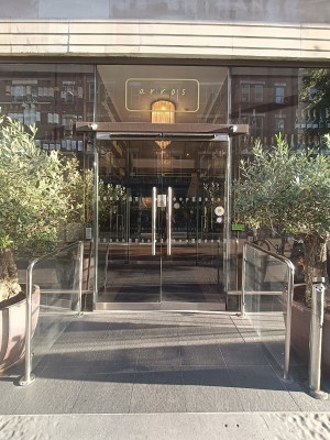 Glass doors with silver vertical metal handles in middle. Pull to open. Glass partitions with silver metal railings on both sides.