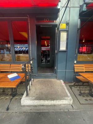 From street, facing straight. One step up before door. Black metal barrier to left. Door ahead.