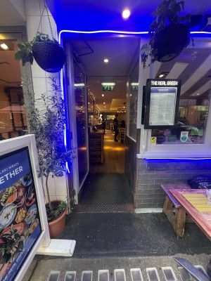 Glass door with white frame ahead. Metal handle to right. Push to open. Sandwich board and planter to left.