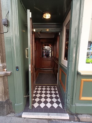 Glass door with green frame. Golden metal handle on right. Pull to open. Blue doorbell on left venue wall.