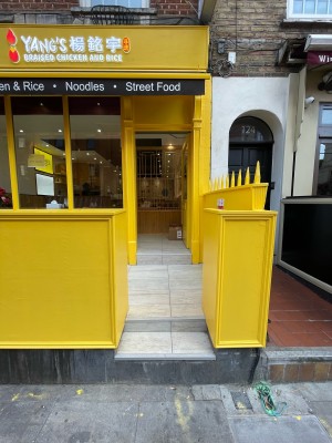 From sidewalk facing venue. Two steps up ahead. Yellow dividing walls either side.