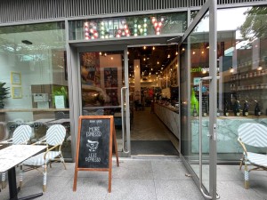 Double glass doors in silver metal frame. Long silver metal handle in centre. Pull from centre to open. Sandwich board left.