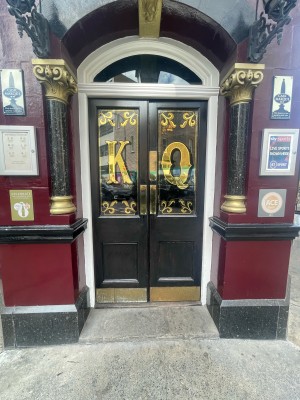 Double black glass and wooden doors ahead. Gold panels to centre. Push to open.