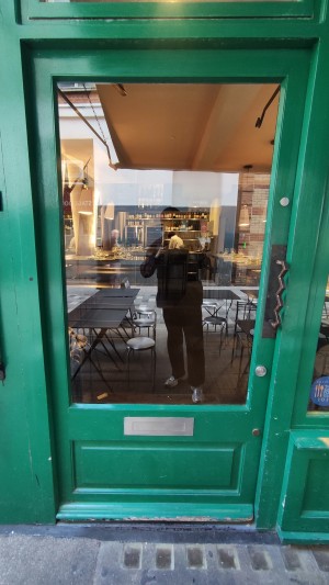 Glass door with green frames ahead. Push to right via brass handle to open.