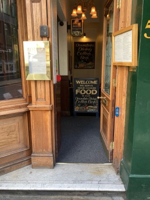 Access via wooden door with glass panel. Push open via handle on left. Blue and white doorbell right of door.