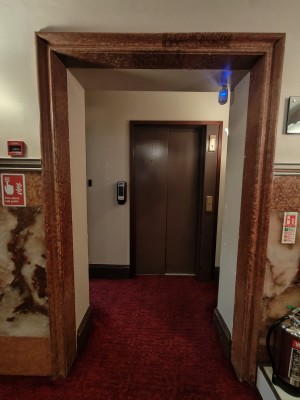 From curved archway facing straight. Brown-framed archway ahead to lift.