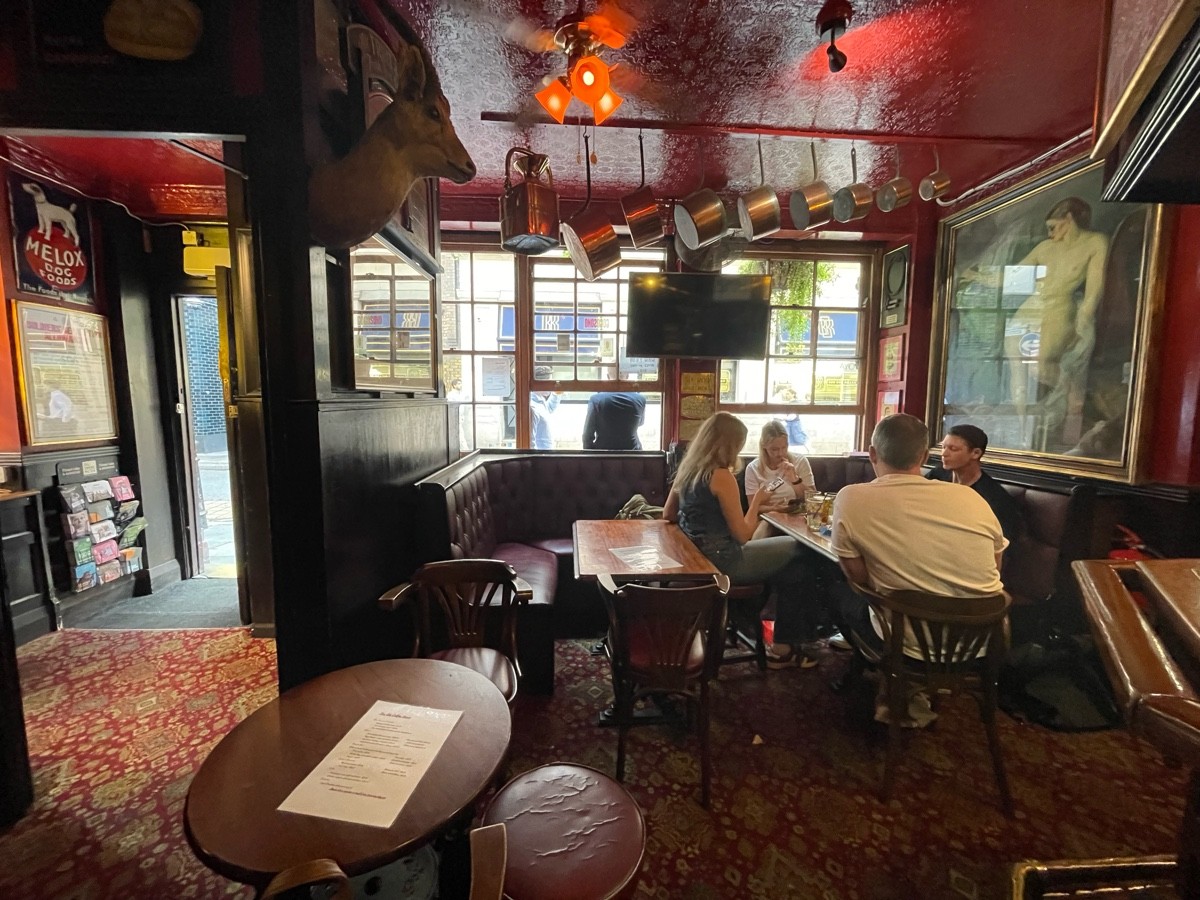 From bar, facing left. Table and chairs ahead. Half booth and chairs along back wall.