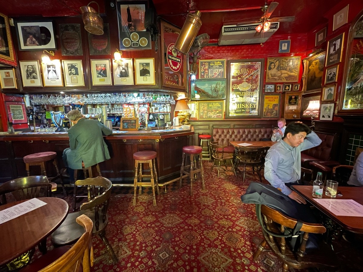 From end of tables and chairs, facing left. Tables and chairs to left and right. Bar with stools along back wall to left. Half booth to back right.