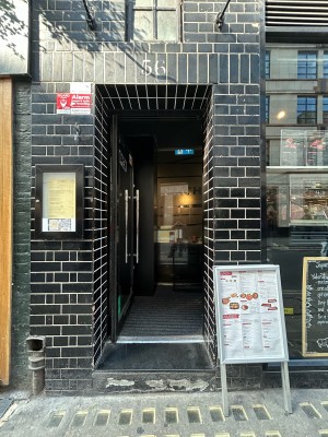 Single glass door with black metal frame and silver metal vertical handle along right. Push to open.