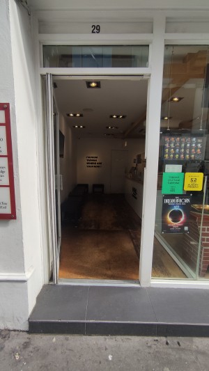 From sidewalk facing venue. One step up to glass door with white frames. Push to right to open via white handle.