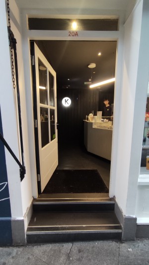 From sidewalk facing venue. 2 steps up to glass door with white frames. Push to right to open via black handle.
