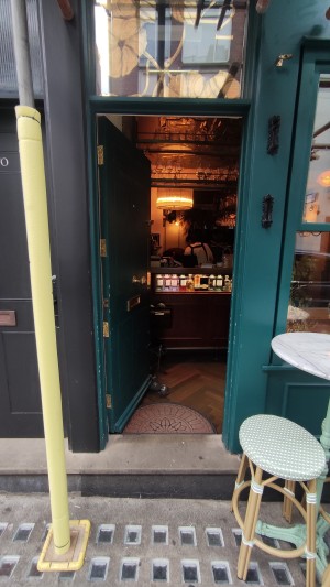 From sidewalk facing venue. One step up to green door. Push to right to open.