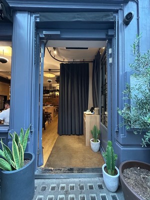 Double glass doors with grey wooden frame. Push from middle to open. Welcome desk on right. Black curtain around back and left. Push right to open.