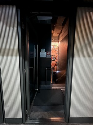 Glass door with grey metal frame. Push from right to open.