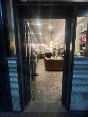 Glass door with black metal frame. Push from right to open.