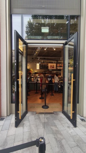 Glass doors with black frames ahead. Pull in centre by yellow vertical handles. Rope barriers to centre of doors.