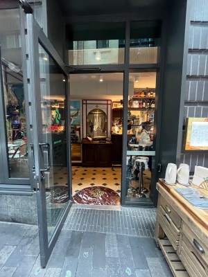 Glass door with grey frame. Pull black handle on right to open. Staff desk before door.