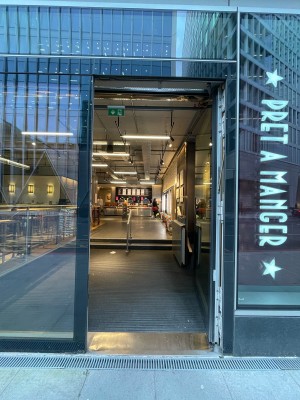 Glass door in black frame. Propped open. Push on left to open. Doormat after door.