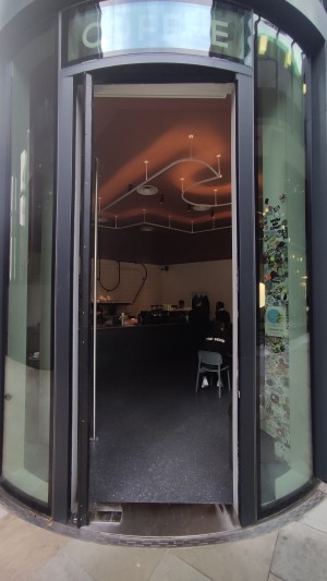 Glass door with black frames ahead. Push metal vertical handle to right.