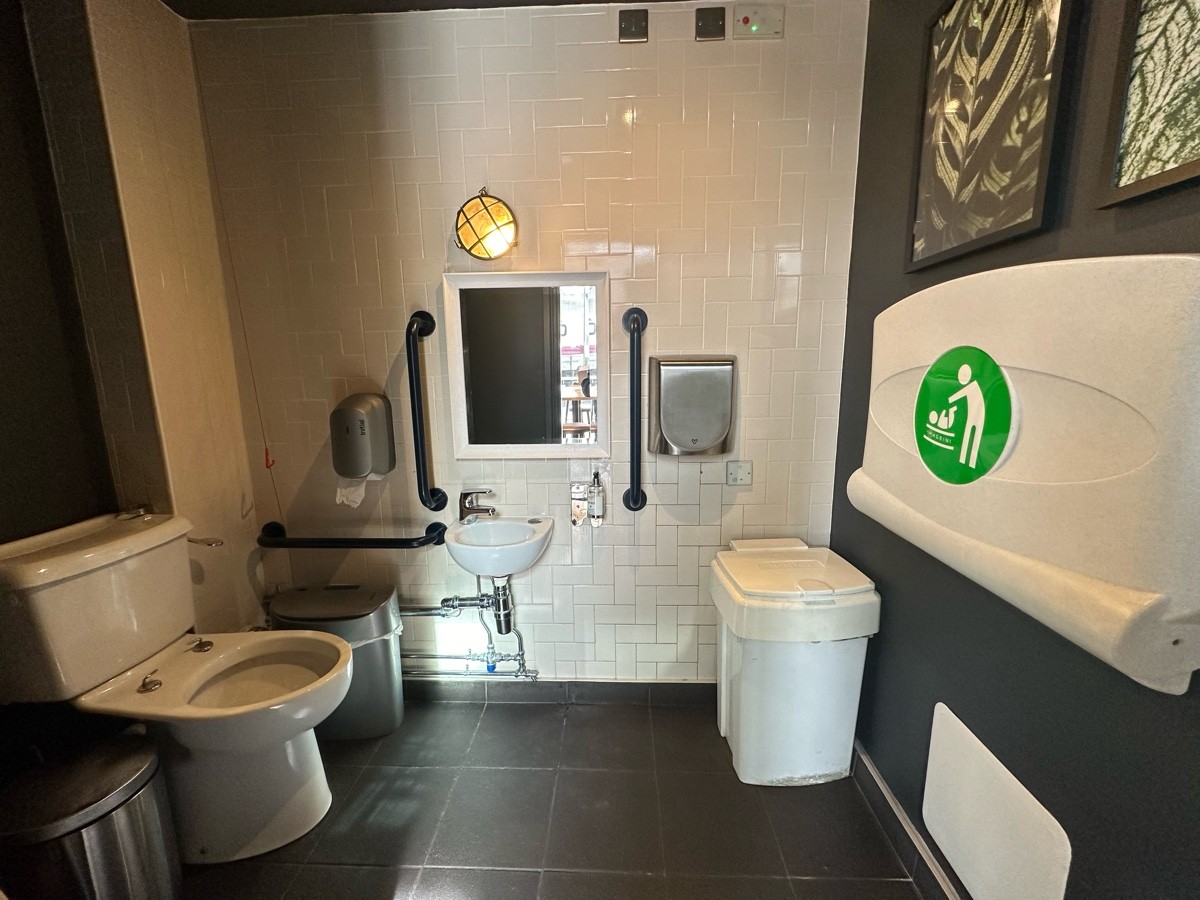 From bathroom door, facing straight. Baby change on right. Sink at back. Toilet to back left.