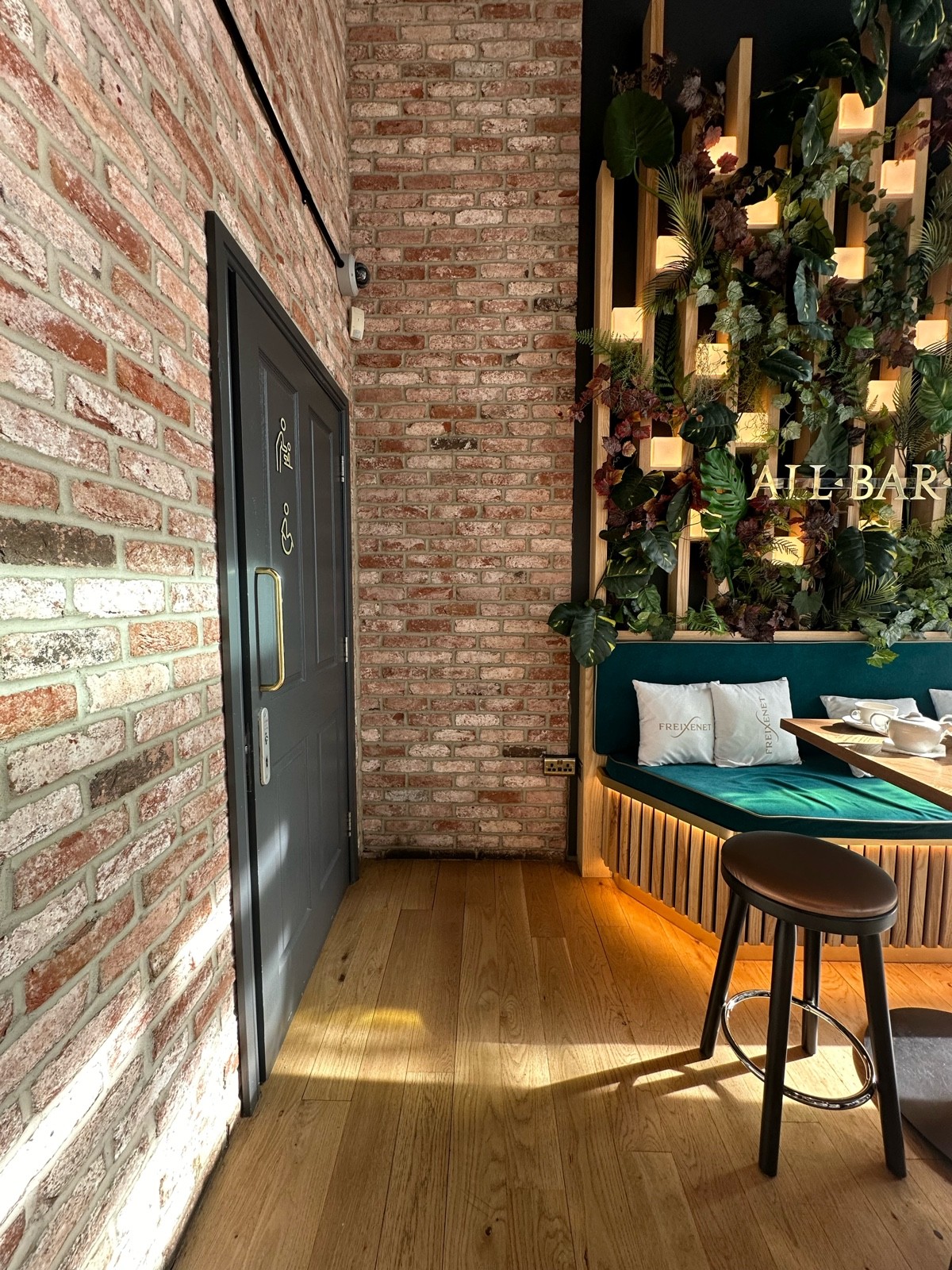 From front-right of main area, facing straight. Half booth with stools on right. Path ahead. Bathroom ahead to left.
