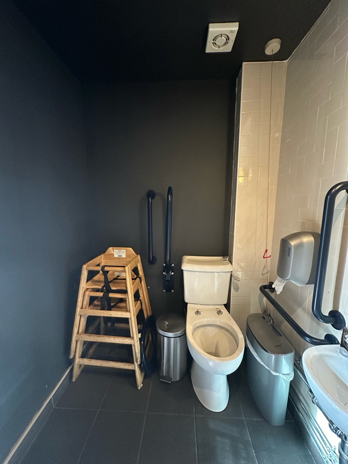 From bathroom door, facing left. Sink on right. Toilet to back right, emergency cord to right of it behind sanitary bin. Obstructed transfer space.
