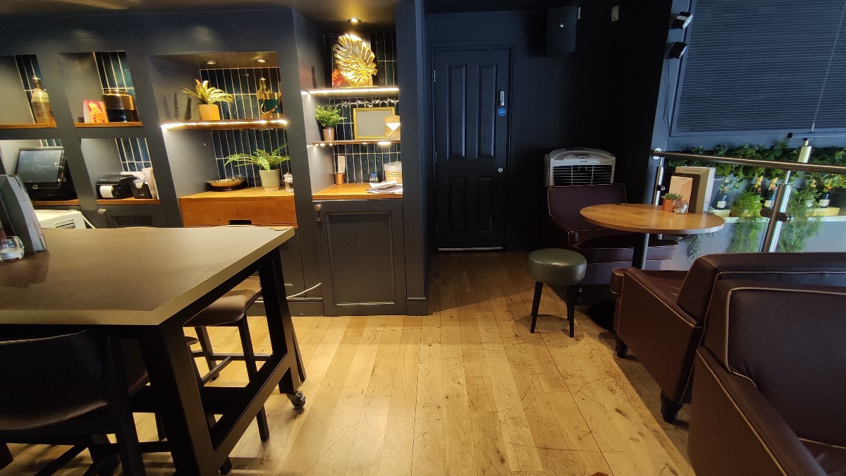 From end of path facing left. High table with stools to left. Staff counter behind it. Path in centre. Tables with armchairs and stools to right.