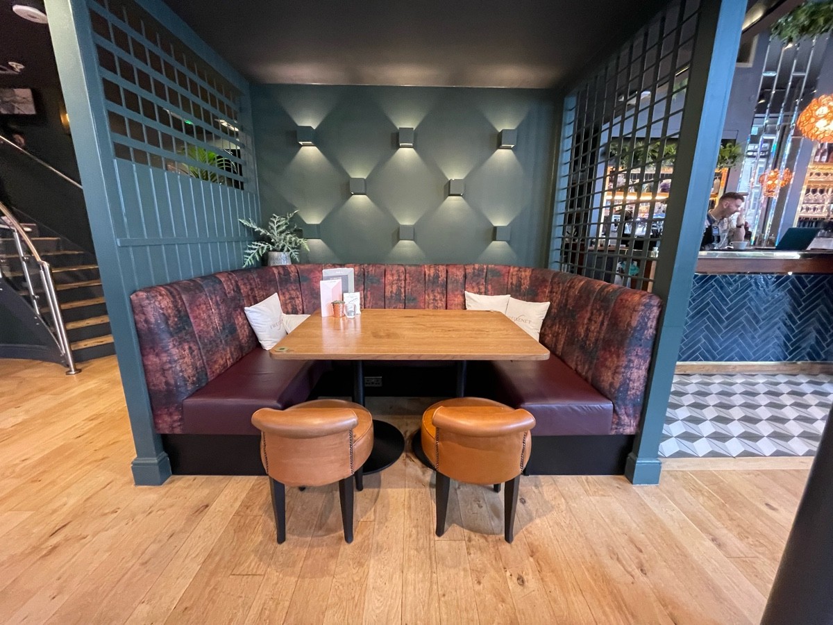 From table and chairs, facing right. Half booth with stools in alcove ahead. Bar to back right.