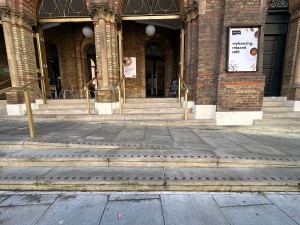 From pavement, facing straight. First set of steps ahead. Gold metal handrail on left.