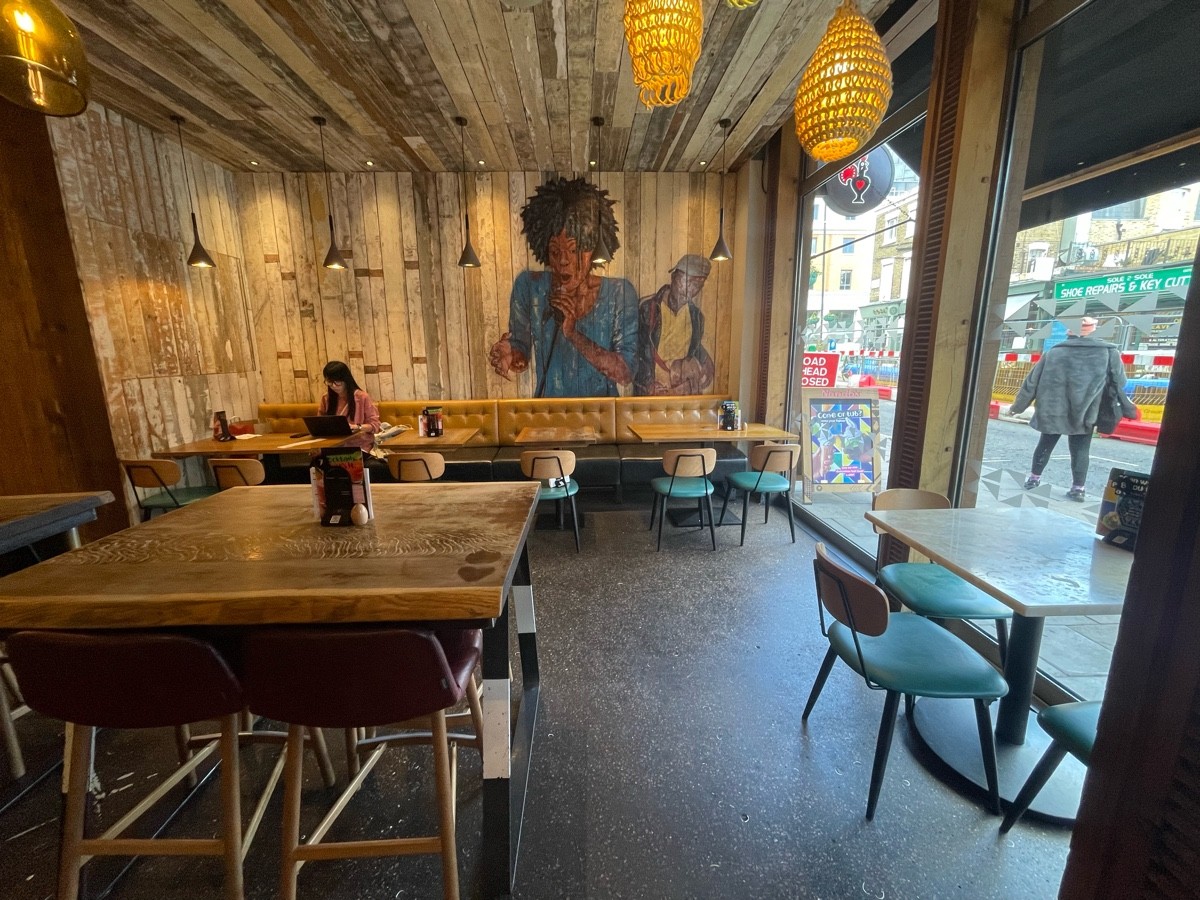 From entrance, facing right. Path straight. Tables and chairs to left and right. Half booth and chairs along back wall.