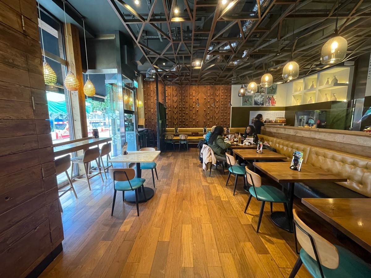 From entrance, facing left. Path straight. High table and stools along left wall. Table and chairs ahead to left. Half booths and chairs along right.