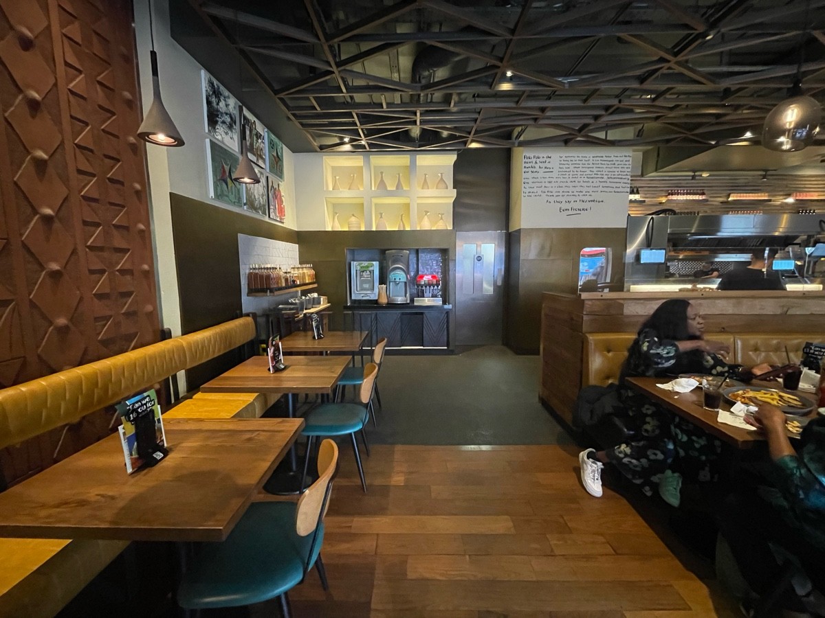 From end of path, facing right. Path straight. Drinks dispenser at back wall. Half booth along left and to right. Service station at back left.
