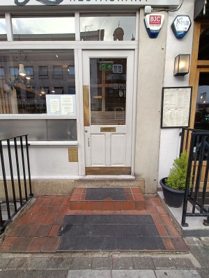 Wooden and glass white door ahead. Gold metal panel on left. Push to open. Steps up before door.