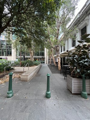 Path to accessible entrance to left of main entrance. Bollard obstructing path in middle. Outdoor area on right ahead.