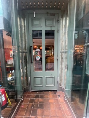 Wooden and glass light green door ahead. Black vertical metal handle to left. Pull to open.