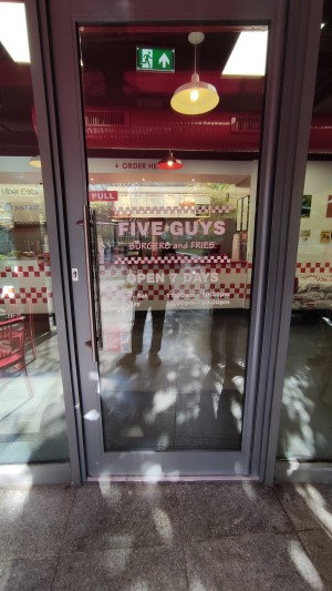Glass door with grey frames ahead. Pull vertical metal handle on left to open.