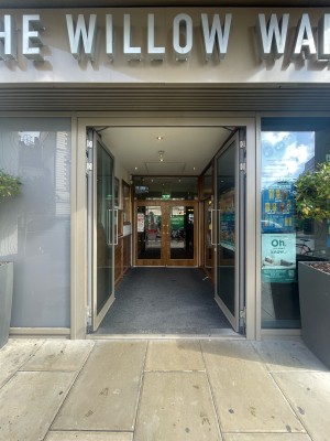 First set of double glass doors with beige frame ahead. Silver vertical metal handles to centre. Push to open.