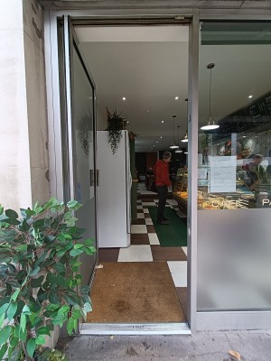 Glass door with silver frame ahead. Silver, metal handle on right. Push to open. Planter to left before door.