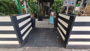 From sidewalk facing venue. Built in ramp ahead going up. Black and white dividers on either side.