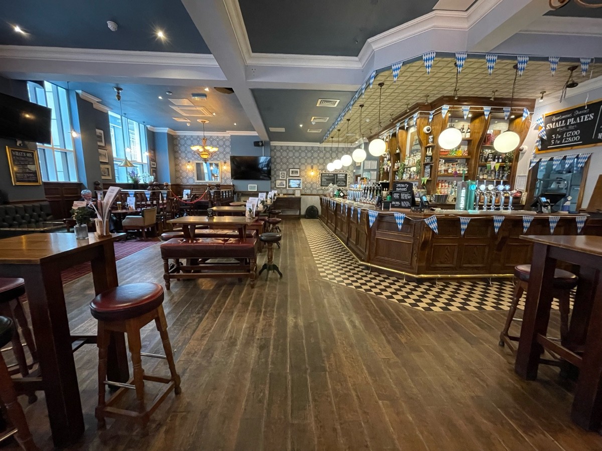 From right of high table, facing straight. Tables, benches and stools to back left. Path ahead. Bar to back right. High tables and stools on right.