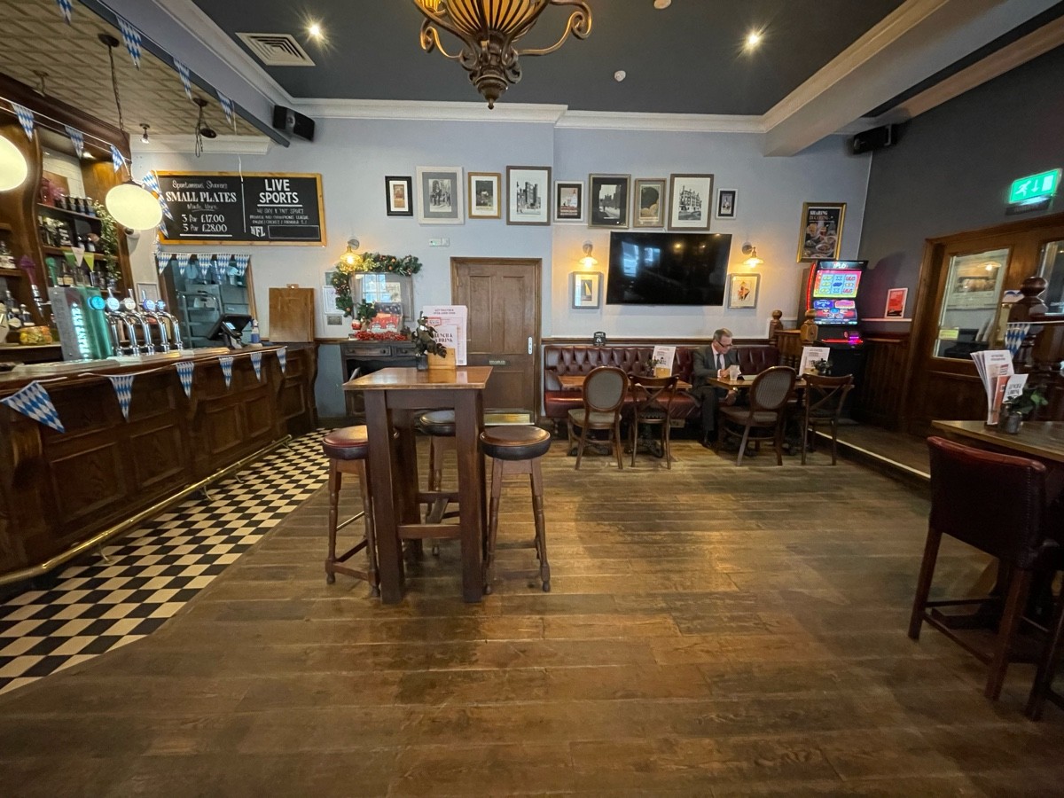 From left of long table, facing straight. Bar to back left. High table and stools ahead. Accessible bathroom beyond. Half booth to back right.